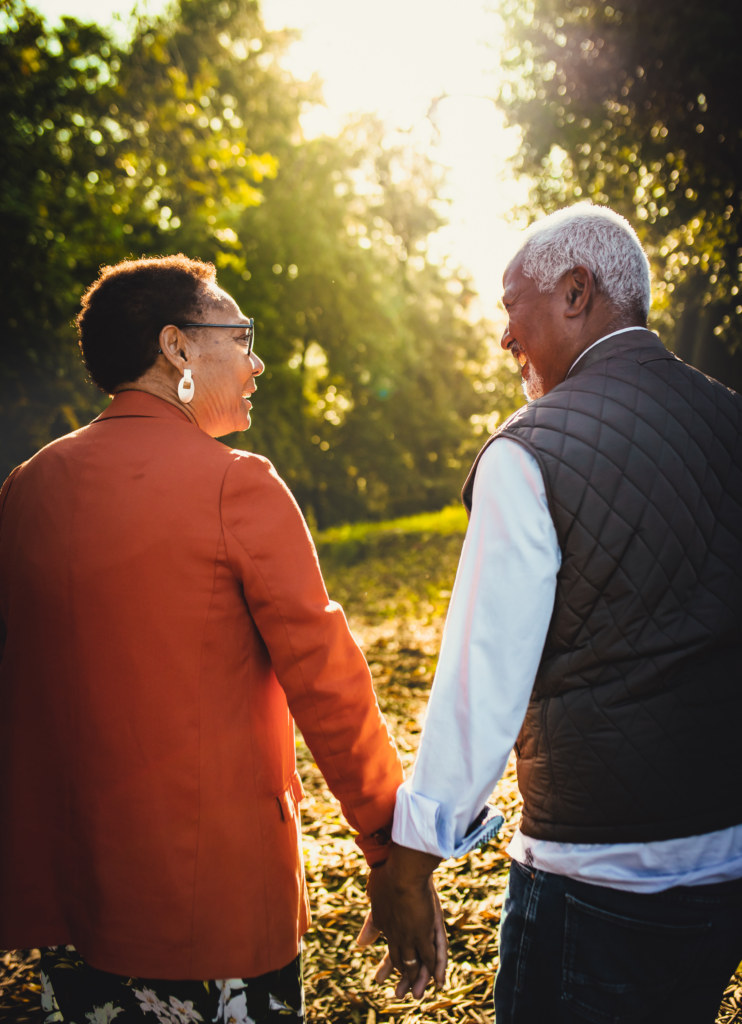 Old black man and old black woman holding hands and walking towards the sunset in the forest.